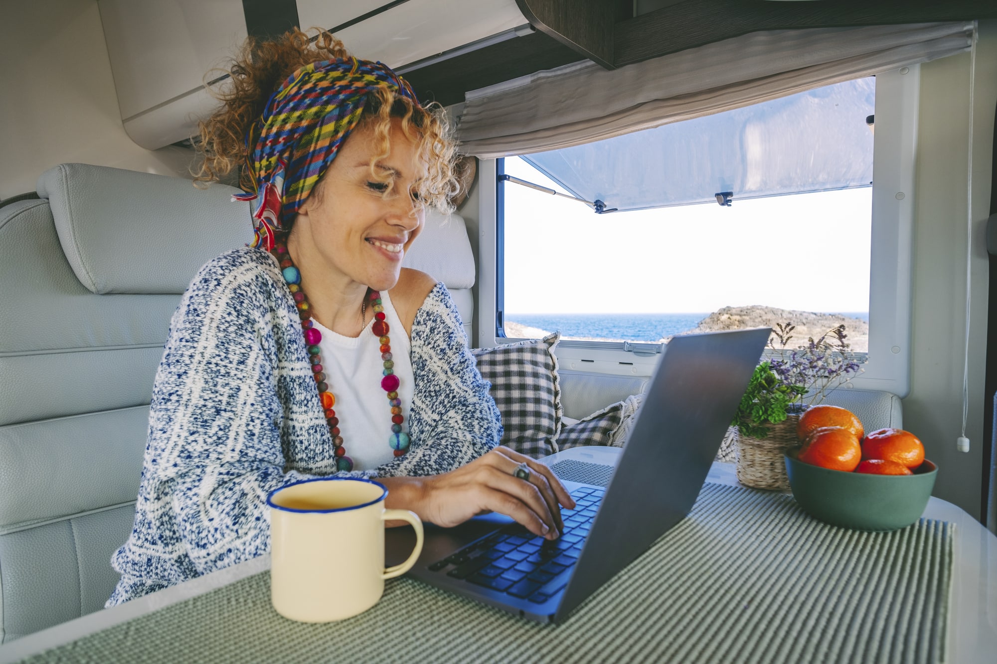 Frau sitzt im Campingfahrzeug am Tisch und arbeitet an ihrem Laptop